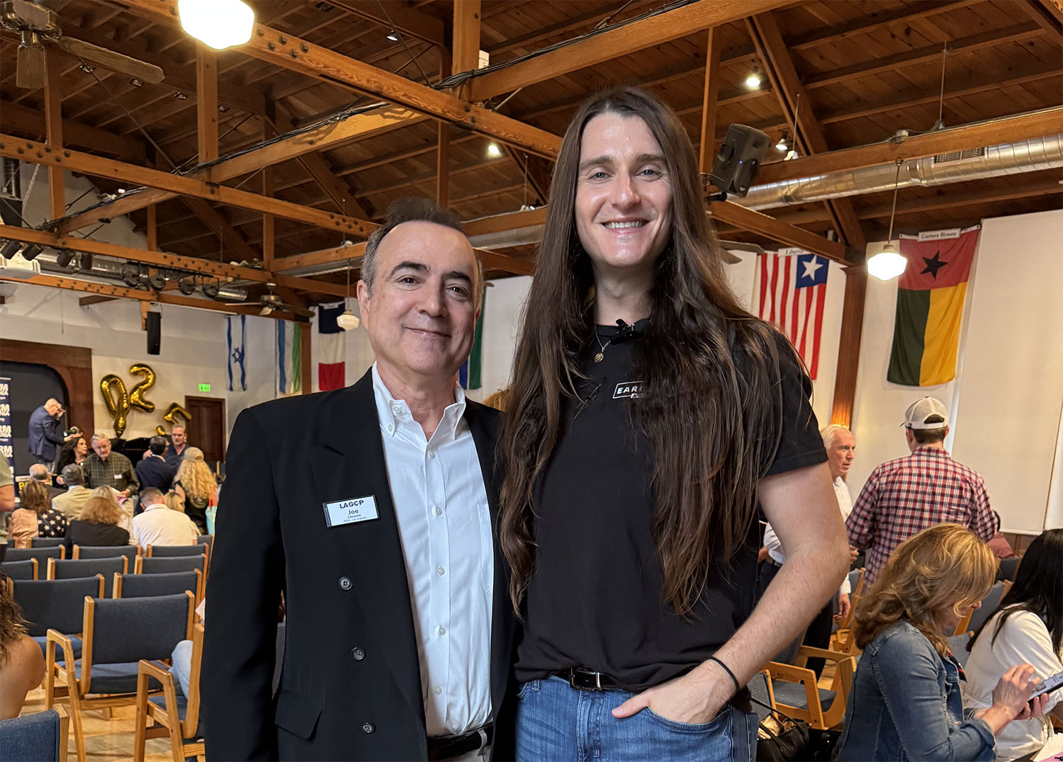 1 man with long hair standing beside a man in coat